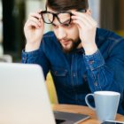 Business man with glasses having eyesight problems confused with laptop isolated on office background.