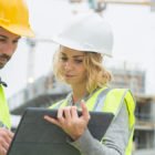 builders in hardhat with tablet at construction